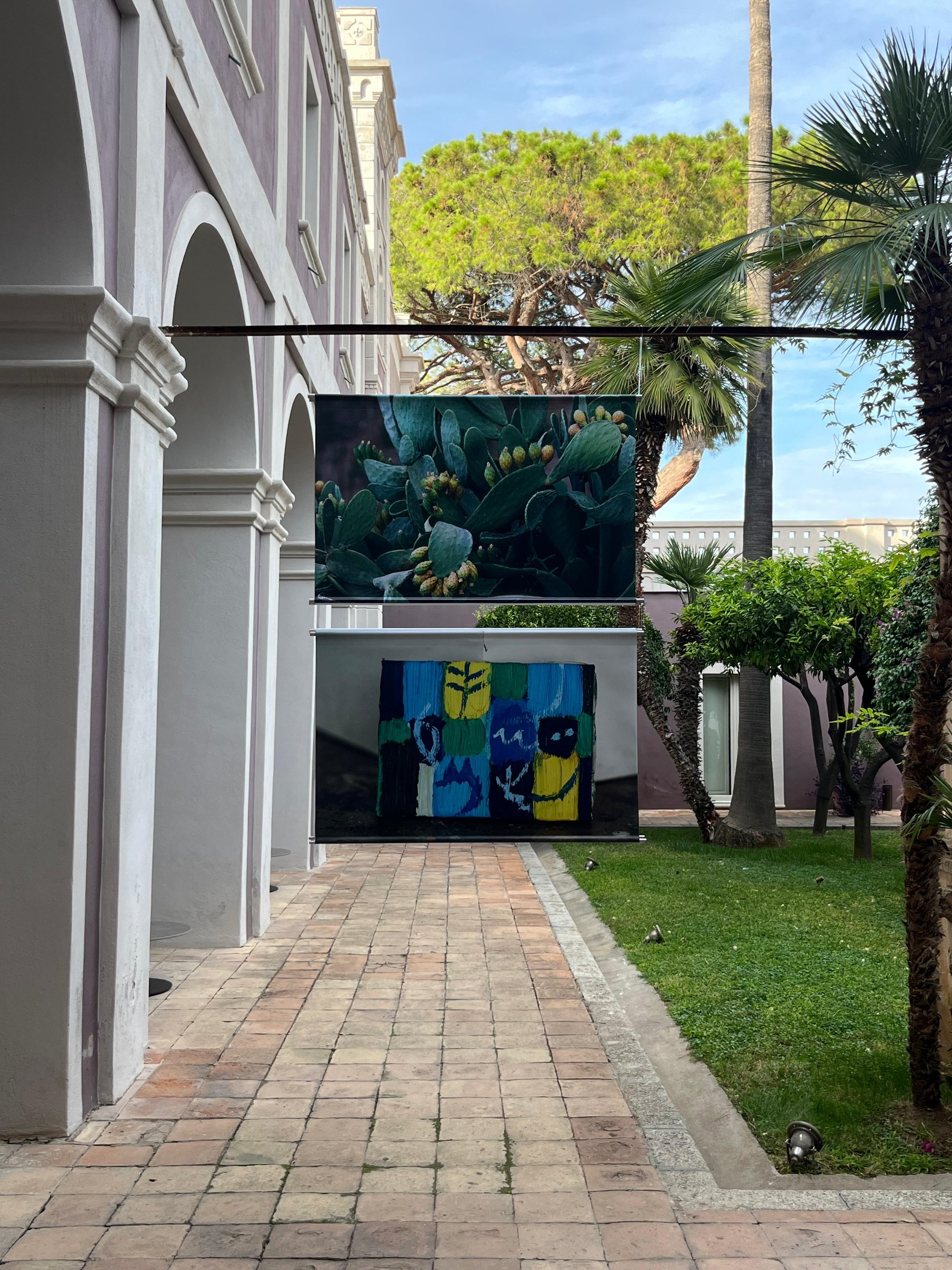 Veduta dell'allestimento: due fotografie appese una sopra l'altra lungo un viale del giardino